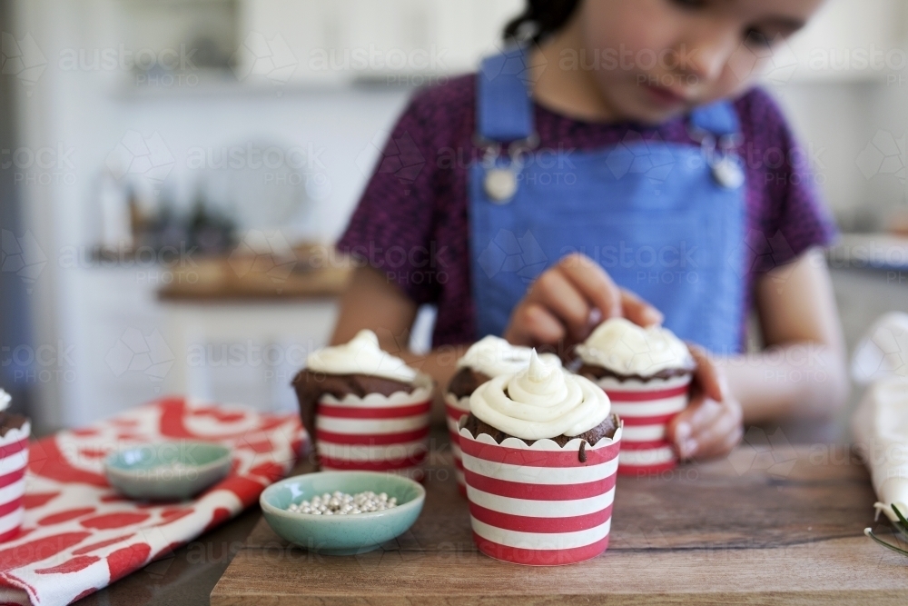 Young girl in kitchen at home decorating christmas cupcakes - Australian Stock Image