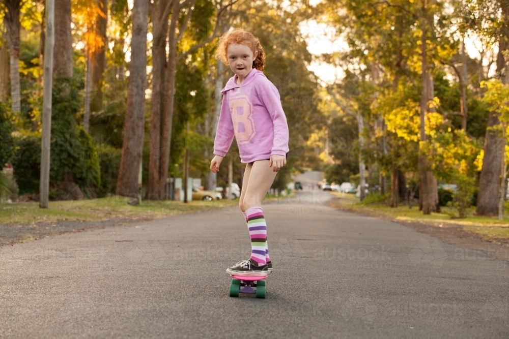 Young girl in long socks riding a skateboard along a road : Austockphoto Young girl in long socks riding a skateboard along a road - Australian Stock Image