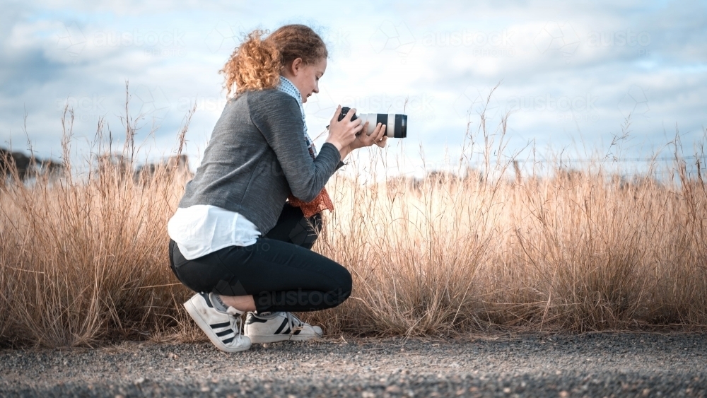 Young girl in profile kneeling taking picture of landscape - Australian Stock Image