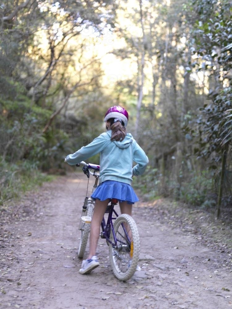 Young girl in purple helmet riding bike on bush track - Australian Stock Image