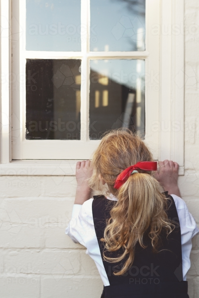 Young girl in school uniform peeking through a window - Australian Stock Image