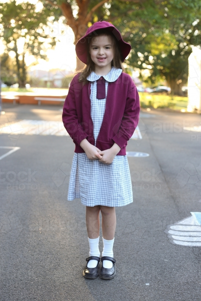 Young girl in school uniform standing outside wearing hat smiling - Australian Stock Image