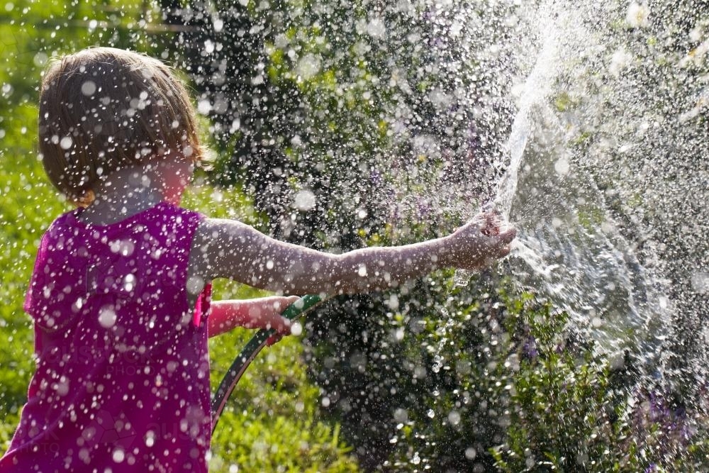 Young girl in sunshine spraying water drops as she waters the garden - Australian Stock Image