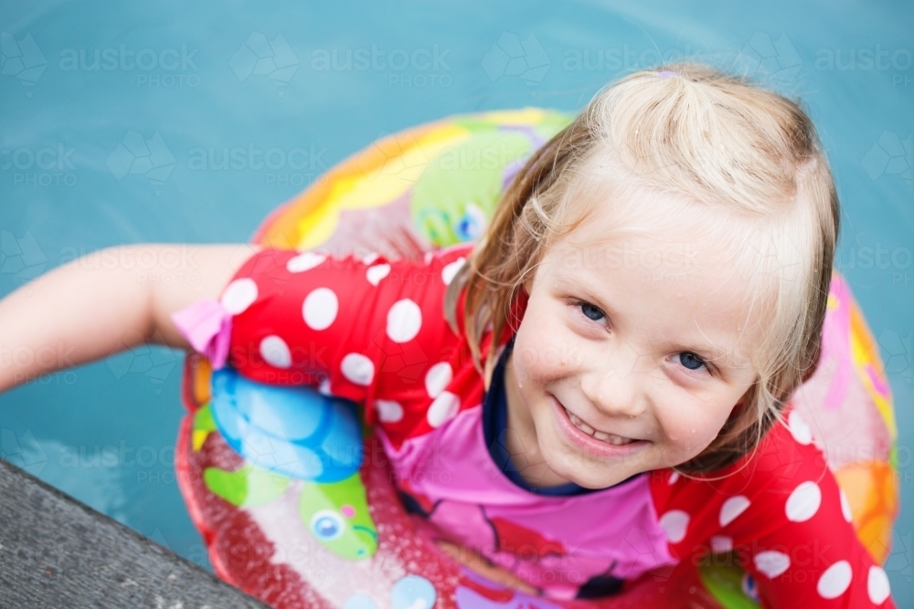 Young girl in swimming pool in a swim ring looking and smiling at the camera - Australian Stock Image