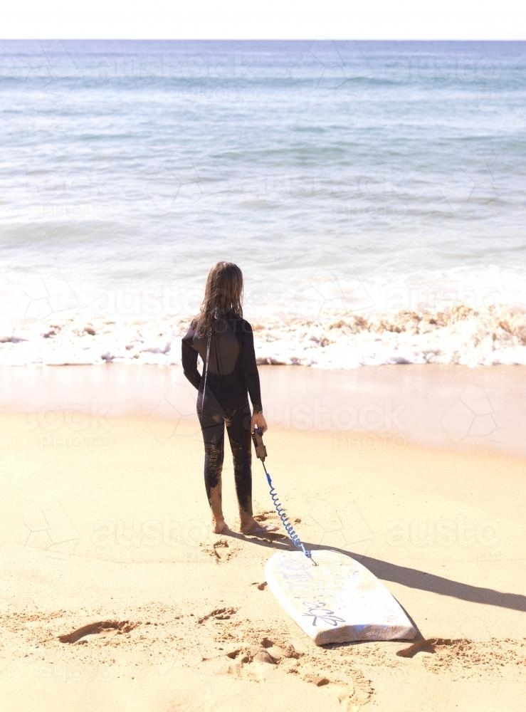 Young girl in wetsuit on beach entering water with body board - Australian Stock Image