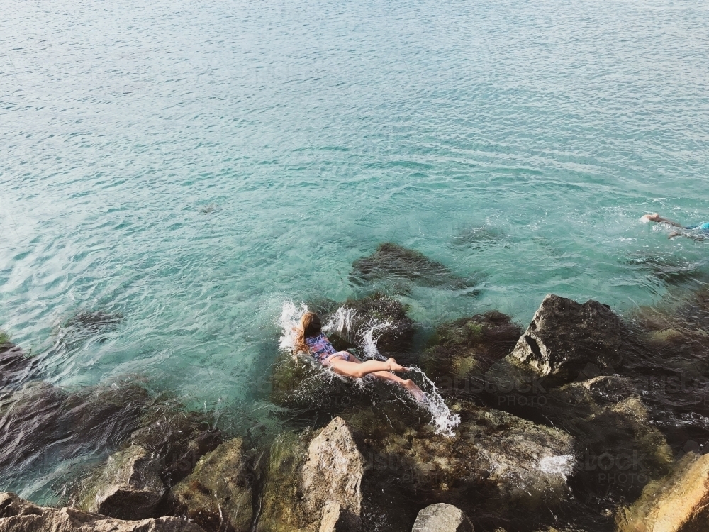 Young girl jumping into ocean from rocks - Australian Stock Image