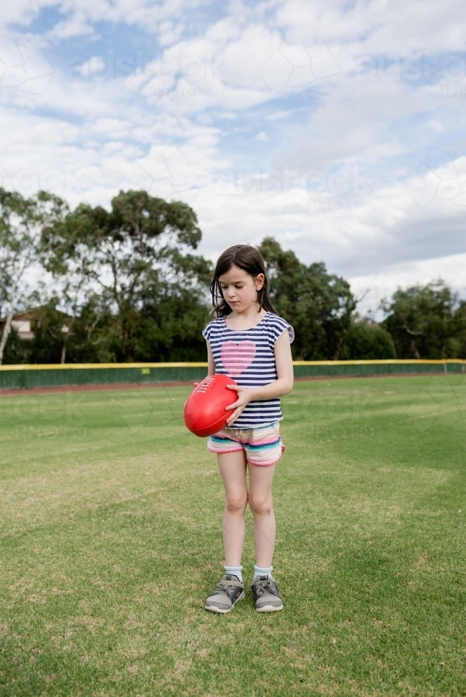 Young girl kicking an AFL ball at the park oval - Australian Stock Image