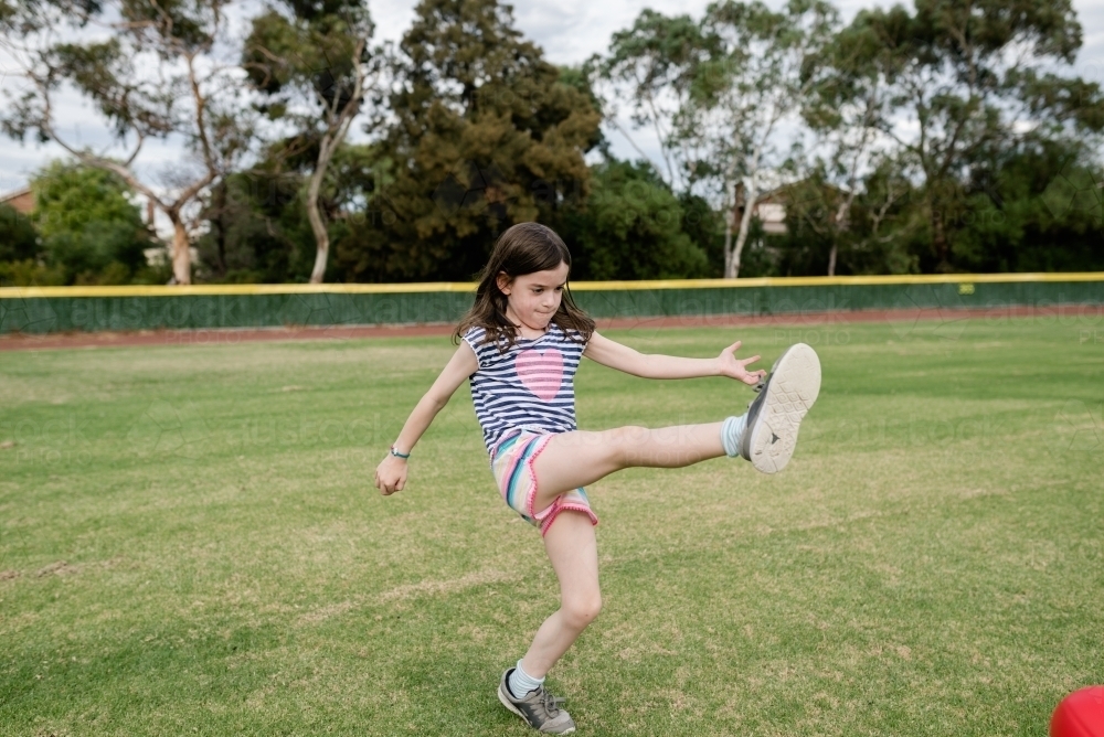 Young girl kicking an AFL ball at the park oval - Australian Stock Image