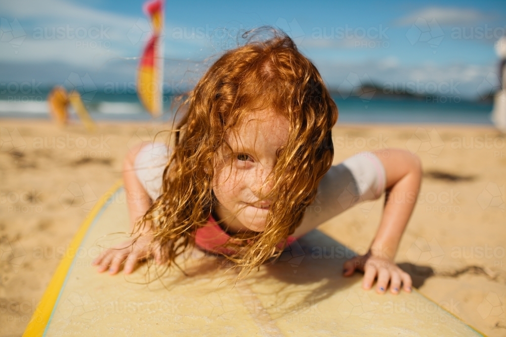 Young girl laying on a surfboard at the beach - Australian Stock Image