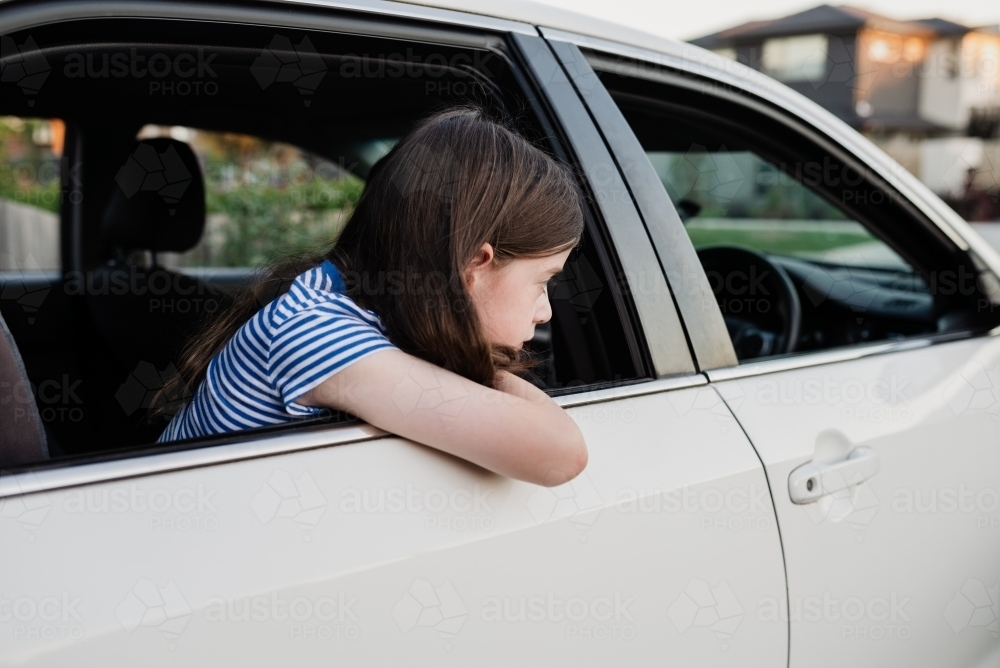 Young girl leaning out the open window of the family car parked in the driveway - Australian Stock Image