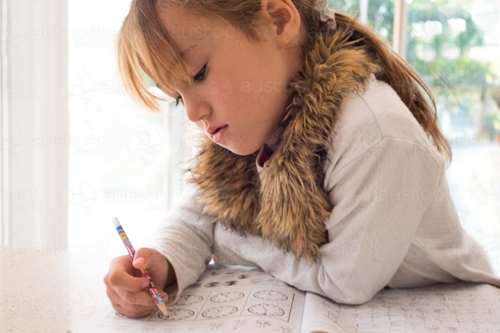 Young girl learning her clock times at home. - Australian Stock Image