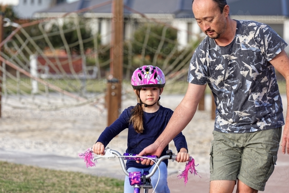 Young girl learning to ride her bike with her dad in the park - Australian Stock Image