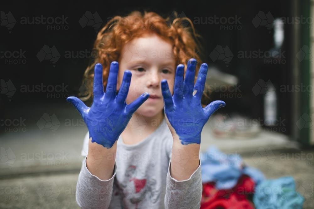 Young girl looking at painted blue hands - Australian Stock Image