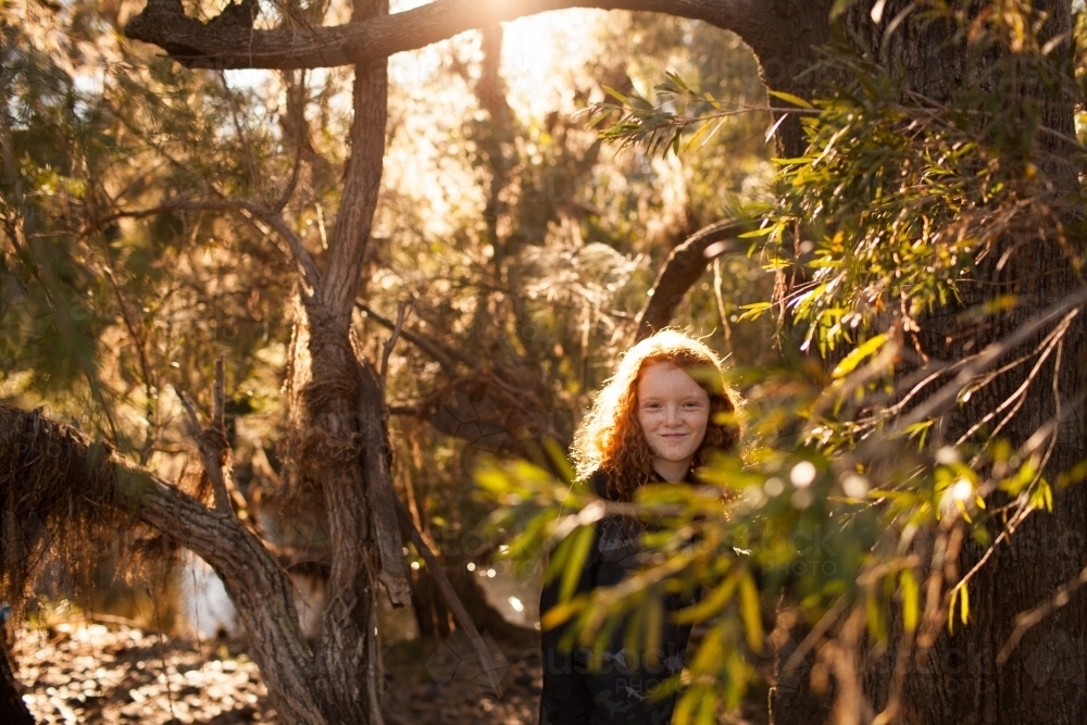 Young girl looking out through trees in afternoon light - Australian Stock Image