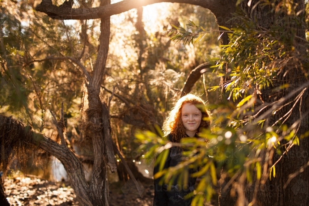 Young girl looking out through trees in afternoon light - Australian Stock Image