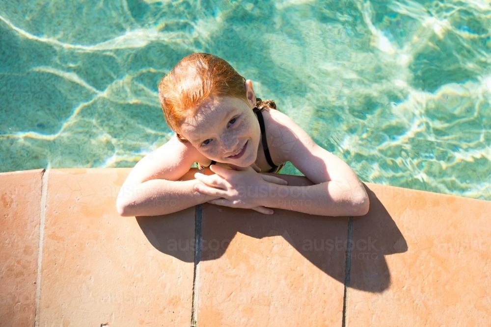 Young girl looking up from the side of a swimming pool - Australian Stock Image