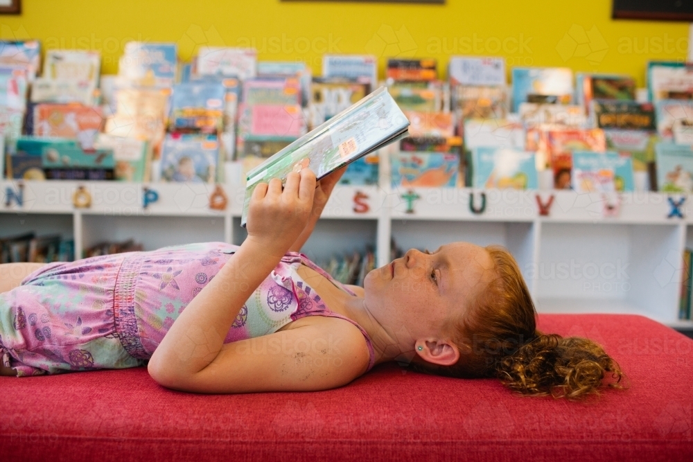 Young girl lying down reading at the Library - Australian Stock Image