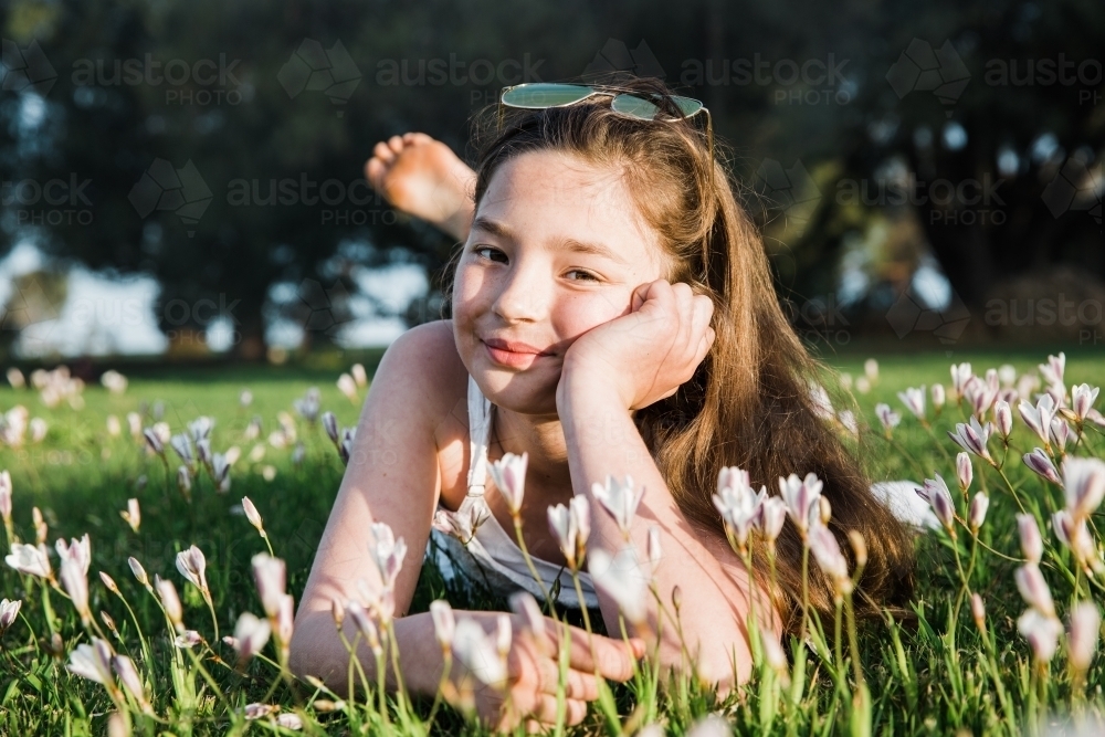 Young girl lying in a flower field smiling at camera - Australian Stock Image