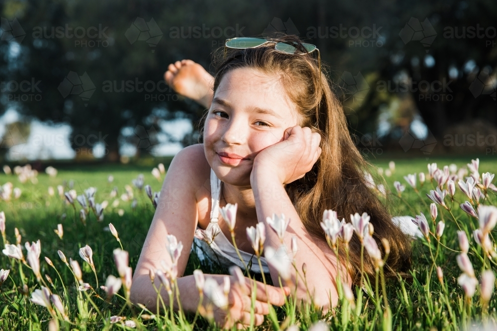 Young girl lying in a flower field smiling - Australian Stock Image