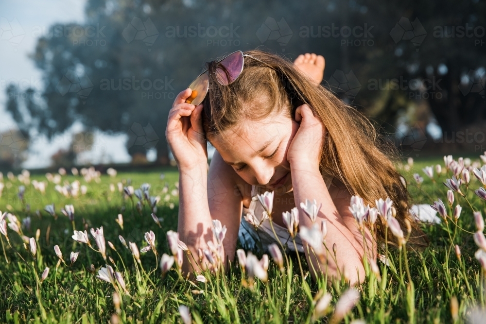 Young girl lying in grass and flowers - Australian Stock Image