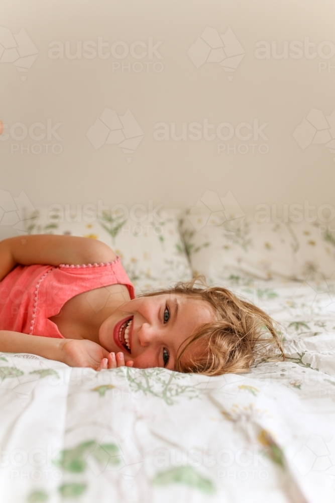 Young girl lying on a bed laughing - Australian Stock Image