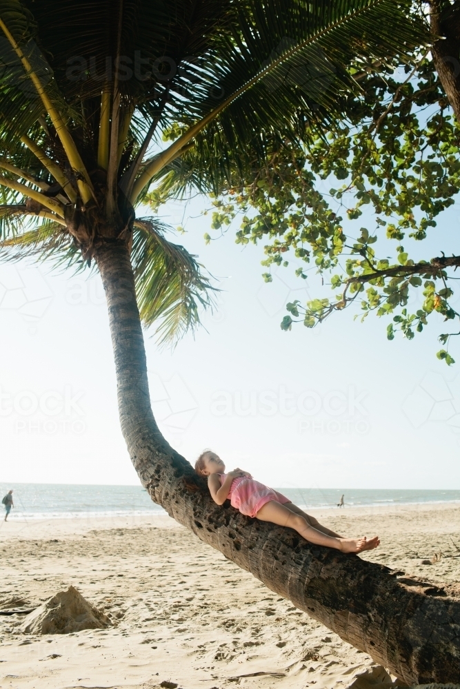 Young girl lying on a palm tree at the beach - Australian Stock Image