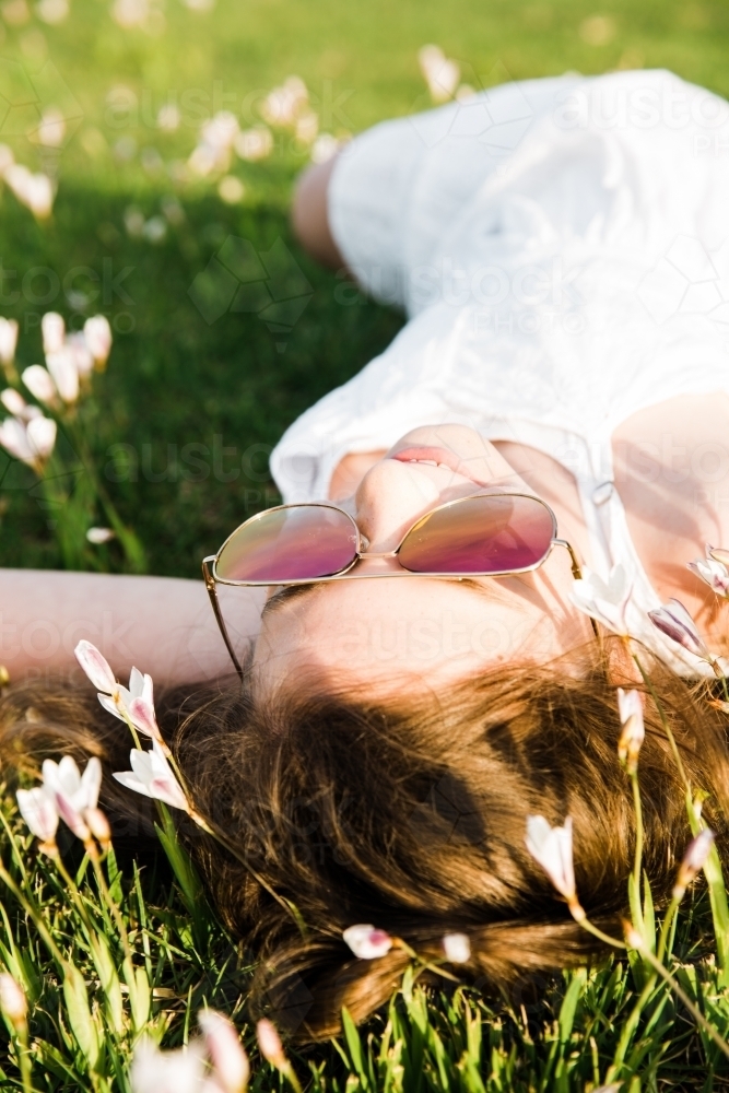 Young girl lying on her back in field of flowers - Australian Stock Image