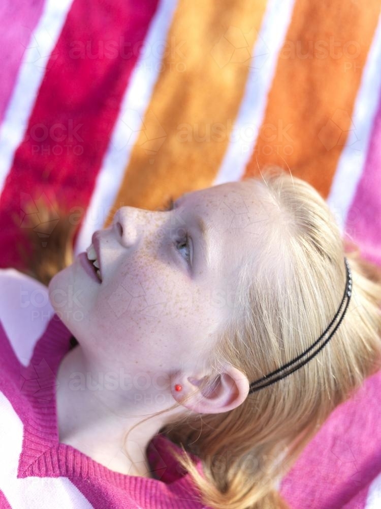 Young girl lying on stripy towel - Australian Stock Image