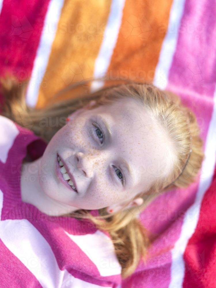 Young girl lying on stripy towel - Australian Stock Image