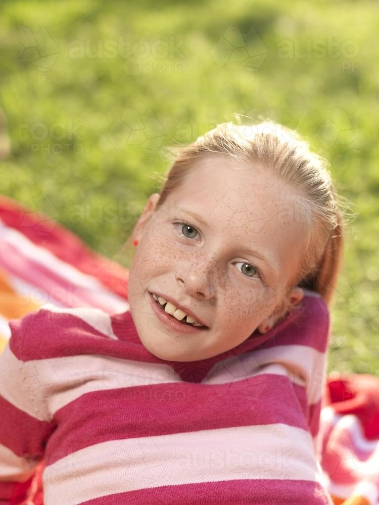 Young girl lying on stripy towel - Australian Stock Image