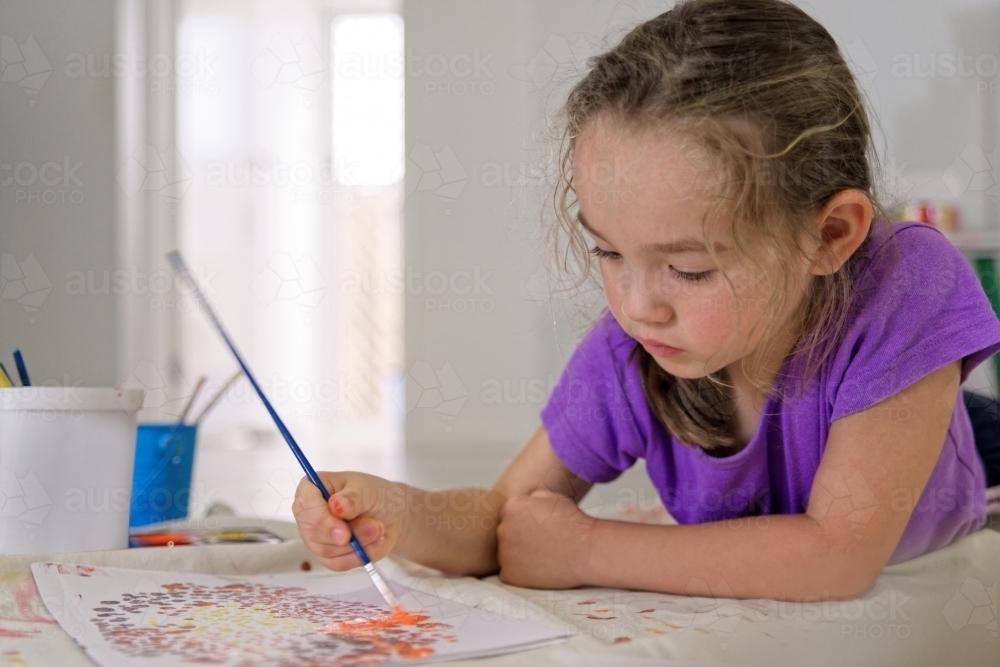 Young girl lying on the floor painting a dot picture with a paint brush - Australian Stock Image