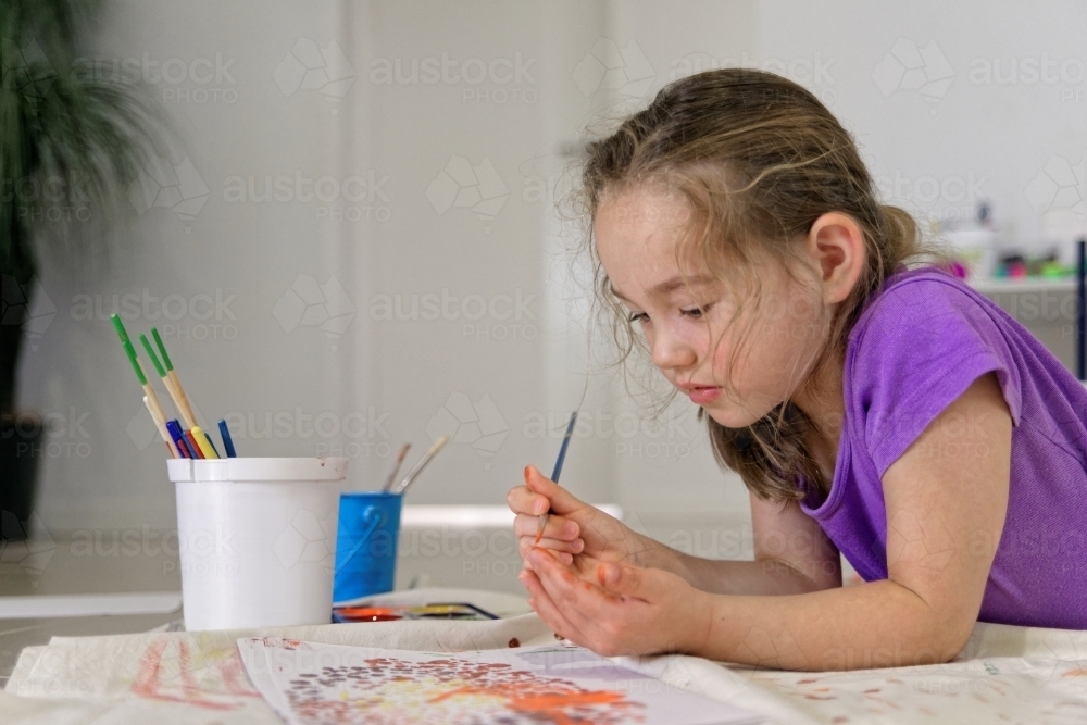 Young girl lying on the floor putting colour on her finger for painting a dot picture - Australian Stock Image
