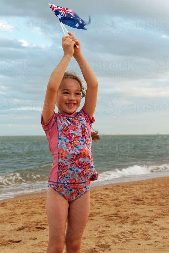 Young girl of mixed race standing and playing on the beach on Australia Day waving small flags - Australian Stock Image