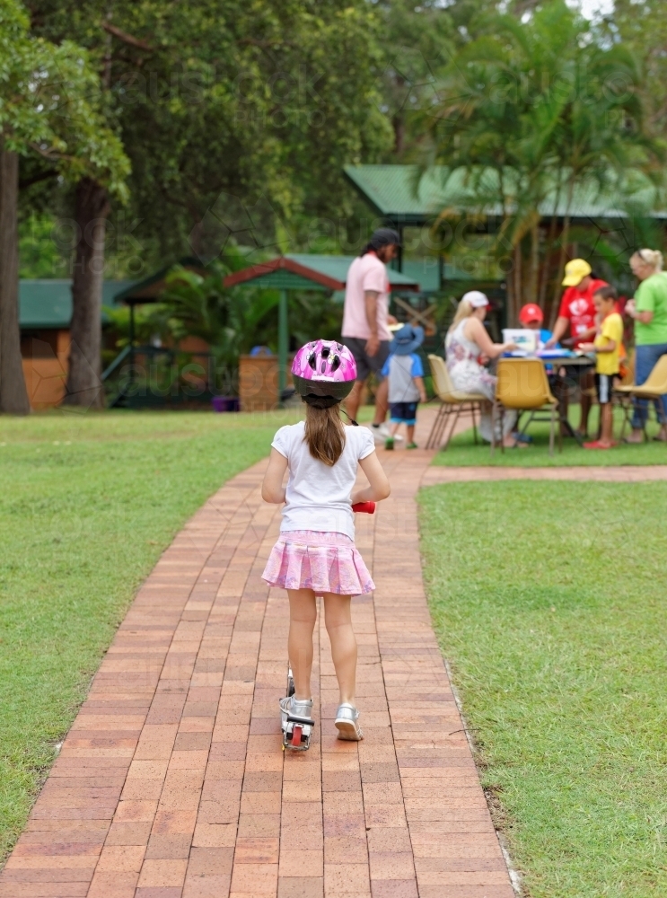Young girl on scooter wearing helmet watching people playing - Australian Stock Image