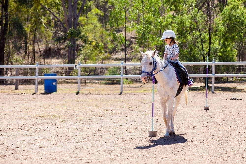 Young girl on white pony pole bending in arena - Australian Stock Image