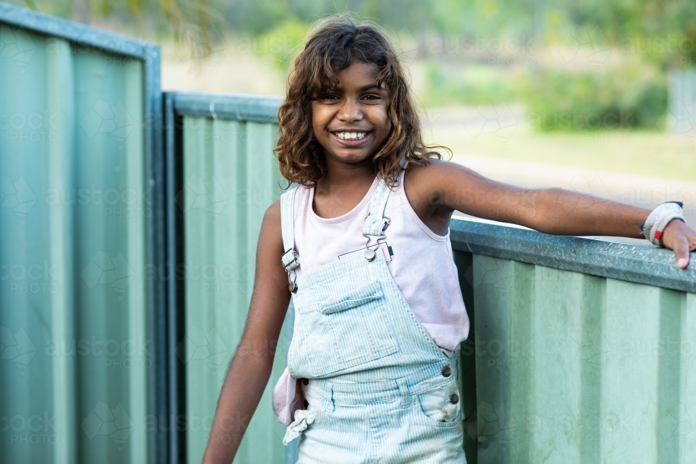 young girl outside near fence looking at camera smiling - Australian Stock Image