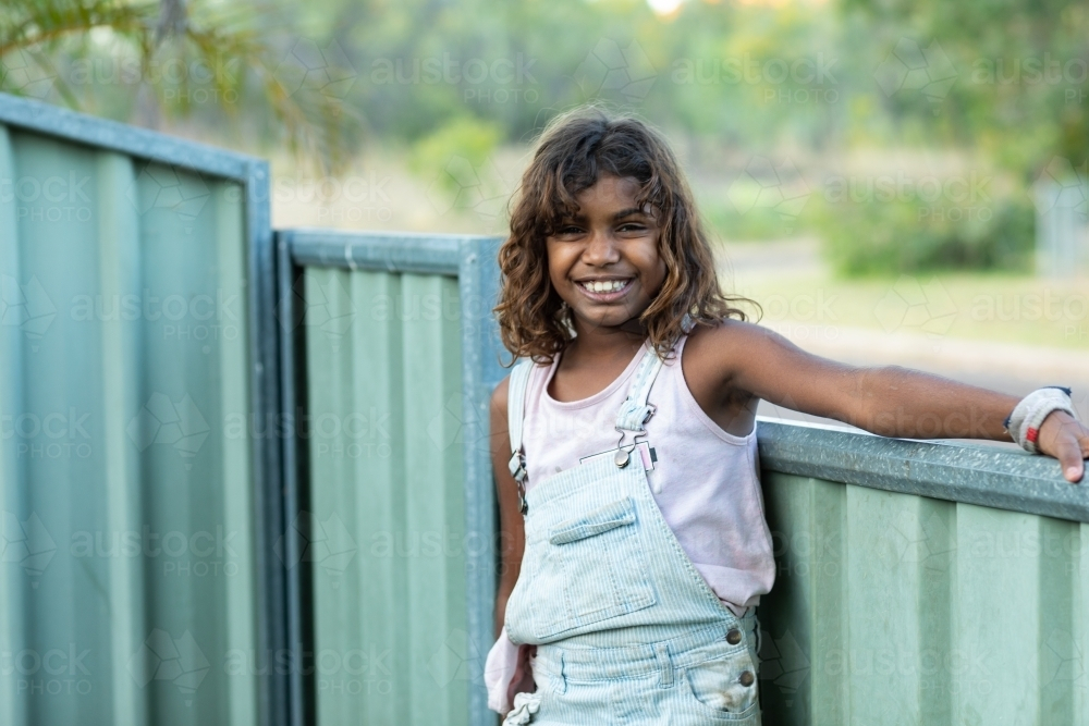 young girl outside near fence smiling - Australian Stock Image