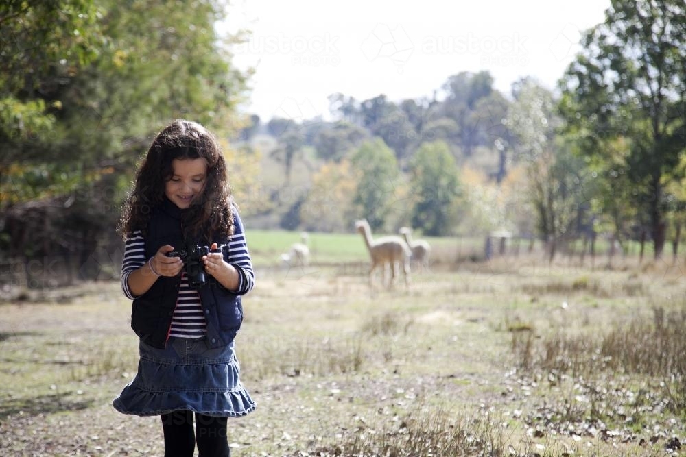 Young girl outside on a farm using a digital camera - Australian Stock Image