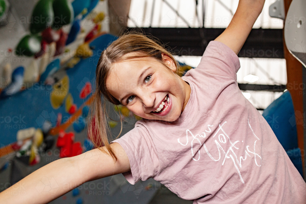 Young girl playfully hanging on the bouldering wall while gripping on the climbing holds - Australian Stock Image
