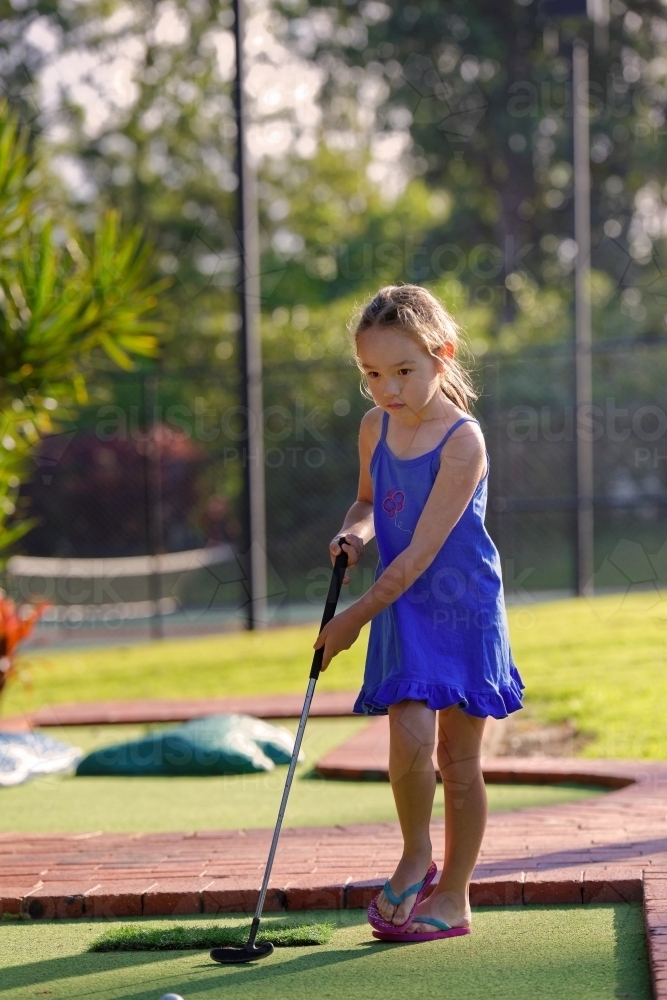 Young girl playing mini golf or putt-put holding golf iron - Australian Stock Image