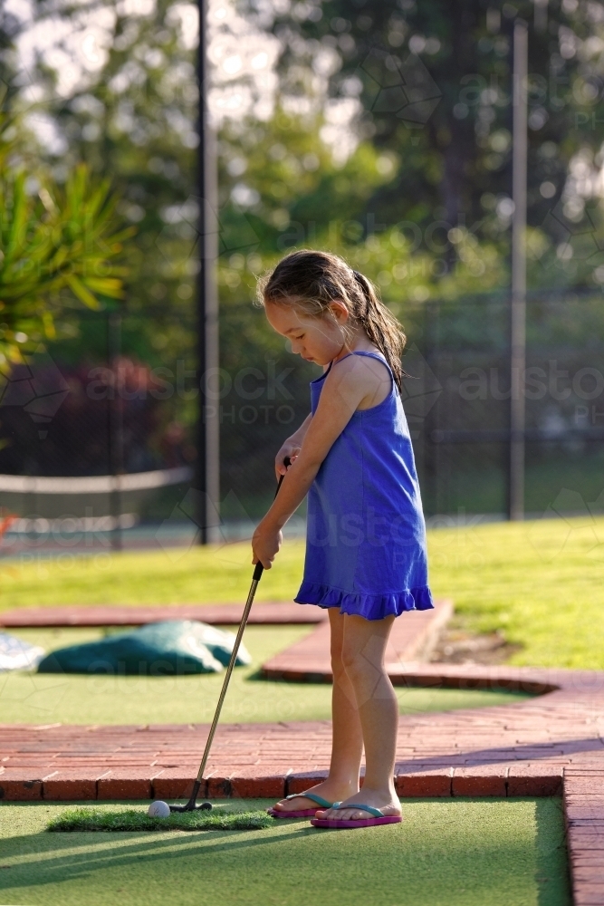 Young girl playing mini golf or putt-putt holding golf iron - Australian Stock Image