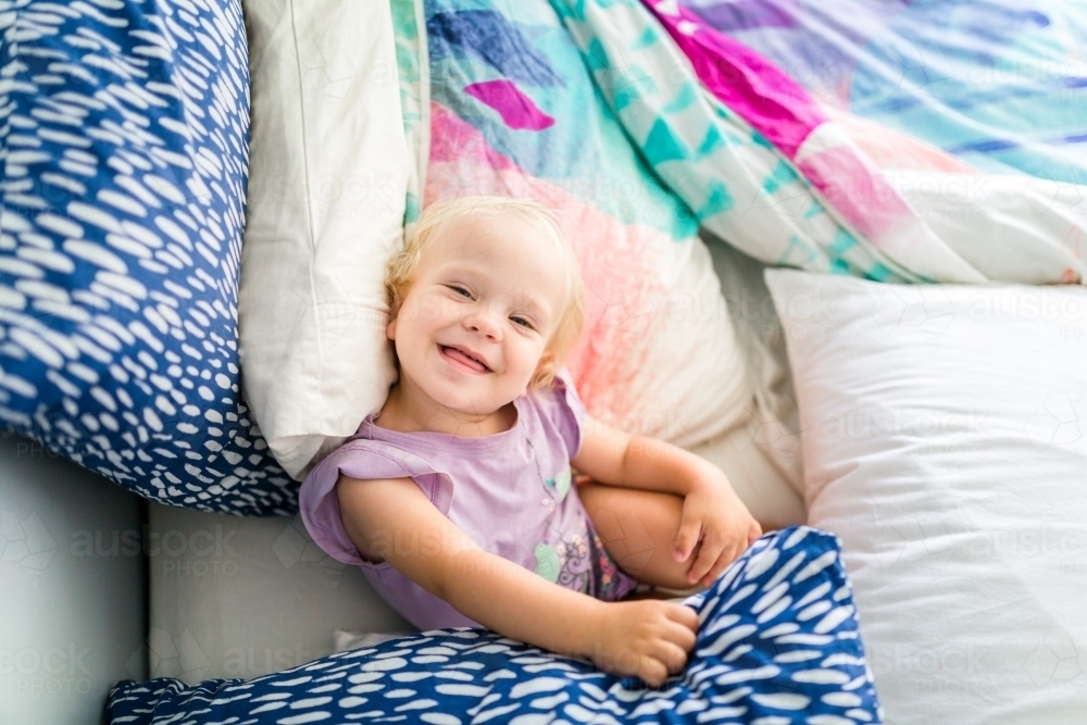 Young girl playing on a colourful bed - Australian Stock Image