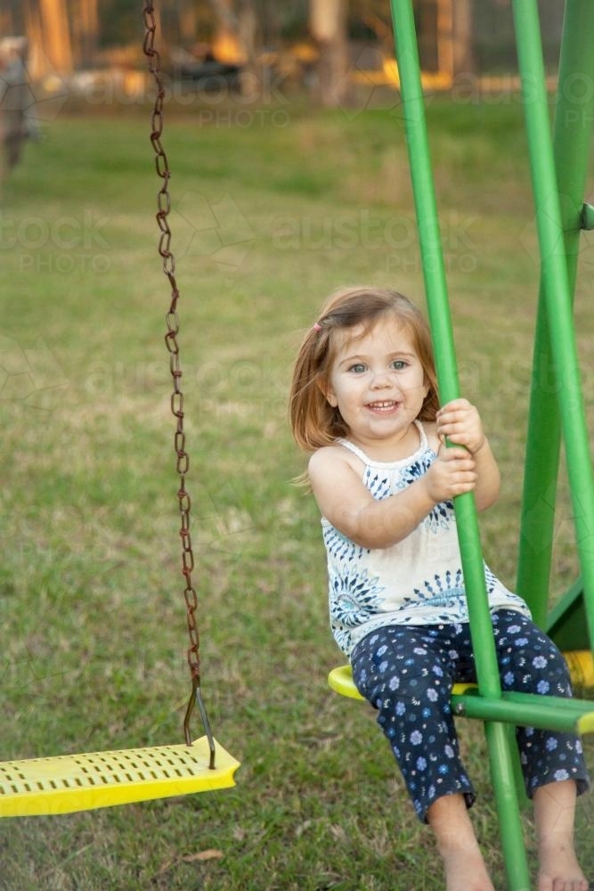 Young girl playing on the swings in the backyard - Australian Stock Image