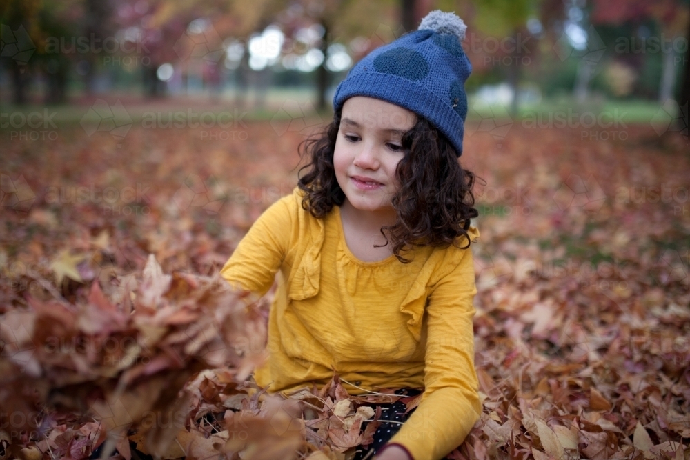 Young girl playing outdoors among piles of autumn leaves - Australian Stock Image