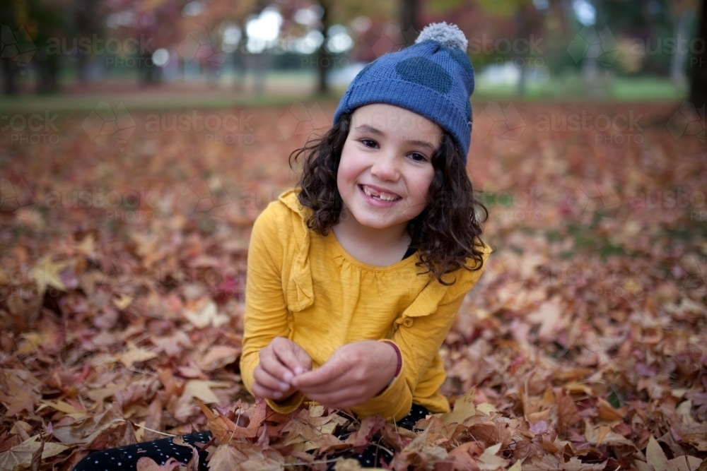 Young girl playing outdoors among piles of autumn leaves - Australian Stock Image