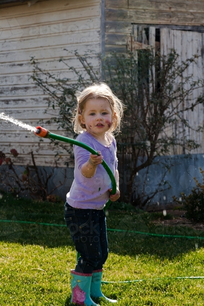 Young girl playing with a hose and water in the backyard - Australian Stock Image