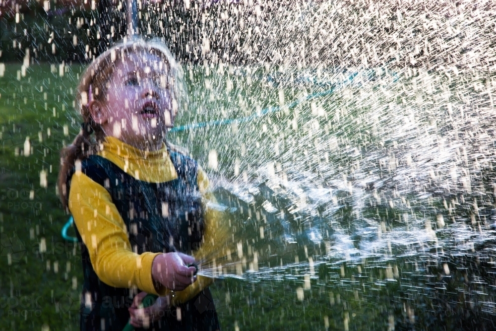 Young girl playing with a hose, water droplets and light - Australian Stock Image