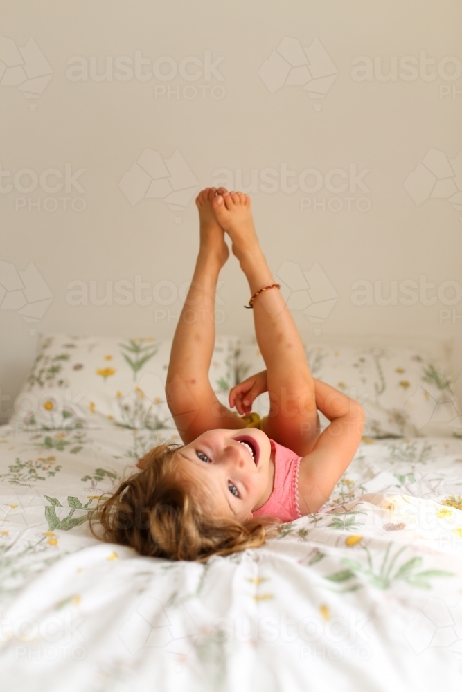 Young girl playing with legs up in the air on a bed - Australian Stock Image