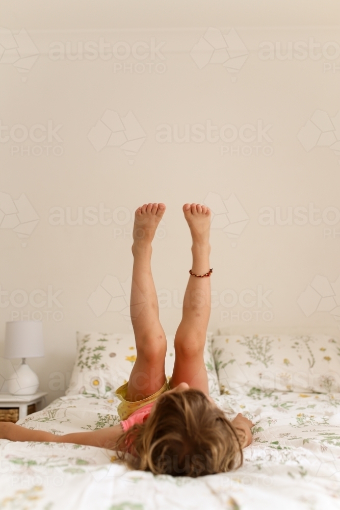 Young girl  playing with legs vertical on a bed - Australian Stock Image