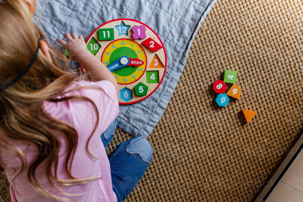 Image of Young girl playing with wooden clock on the floor - Austockphoto